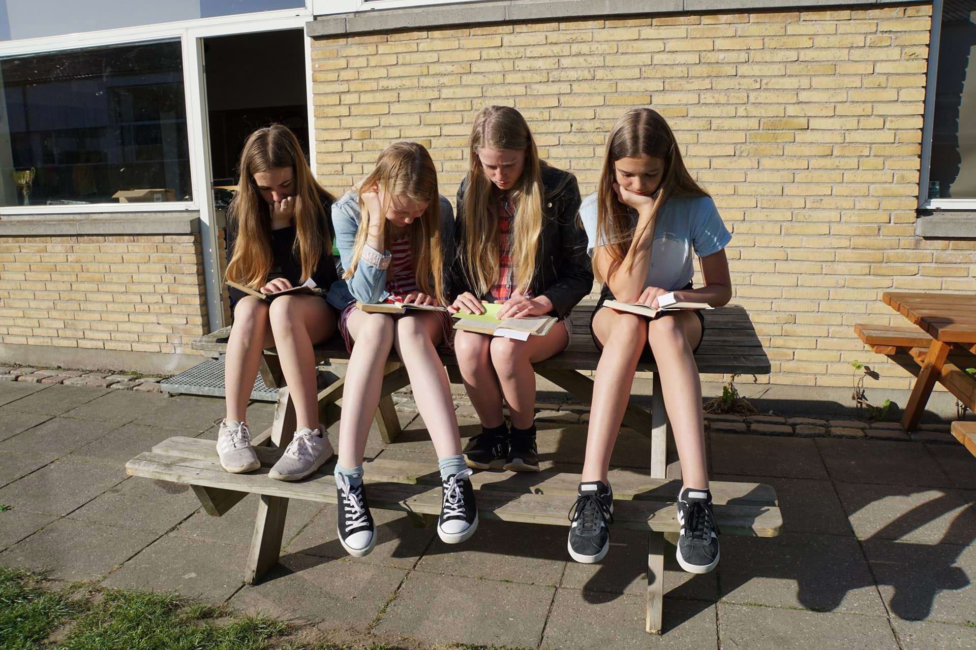 Fire piger sidder i solskinnet og læser